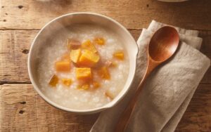 Photograph of a bowl of warm congee topped with sweet potato cubes, with a wooden spoon resting on a linen napkin — a classic Spleen-nourishing food in Traditional Chinese Medicine (AI-generated)